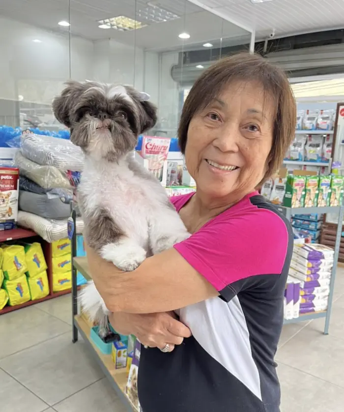 Tutora sorrindo com shih tzu no colo na loja da Azzurra